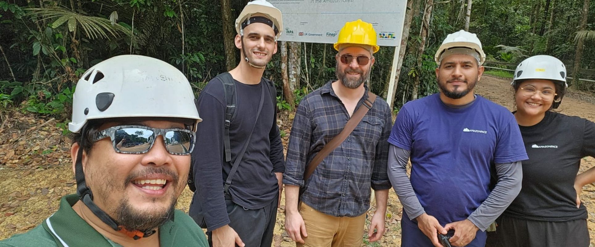 Five people stood together in the Amazon rainforest. They are all wearing hard hat.